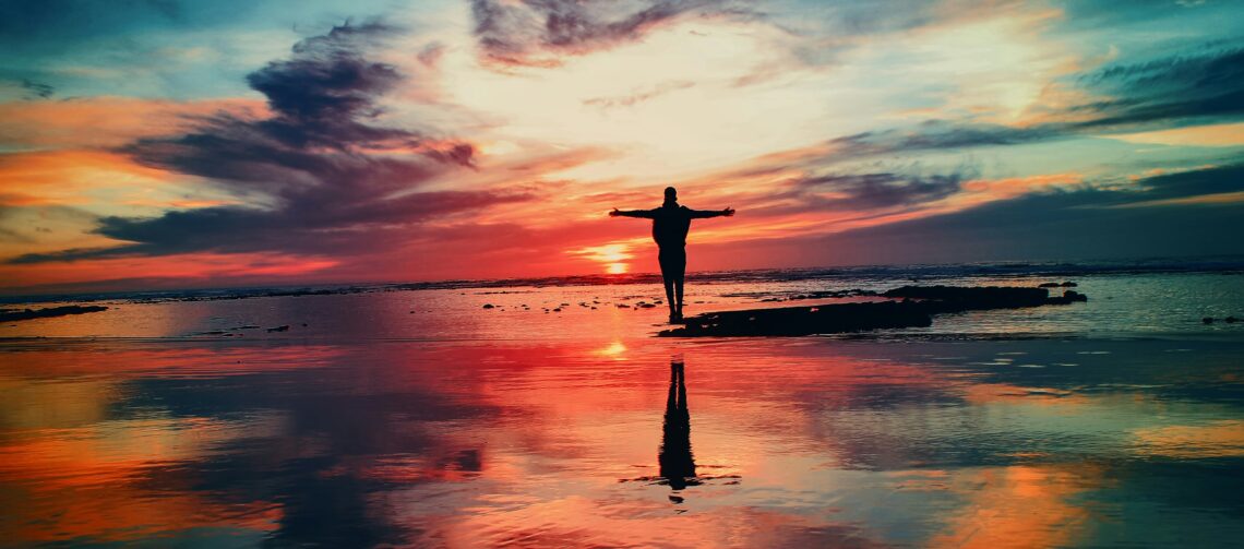 Persoon met uitgestrekte armen op strand bij zonsondergang