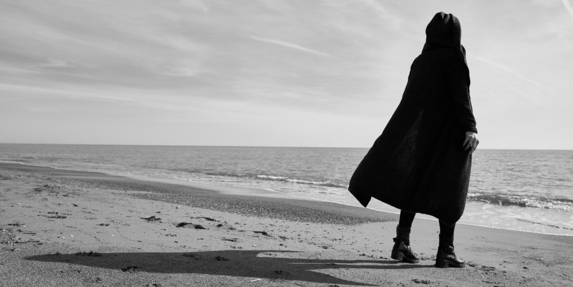 Figuur in een cape die vanaf het strand uitkijkt op de zee