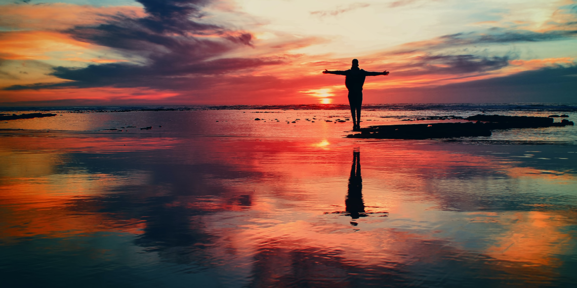 Persoon die bij zonsopgang met gespreide armen op het strand staat