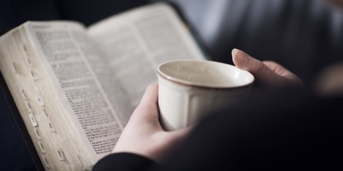 Vrouw die de bijbel leest met een kopje koffie Een vrouw die de bijbel leest en bestudeert met een kopje koffie.