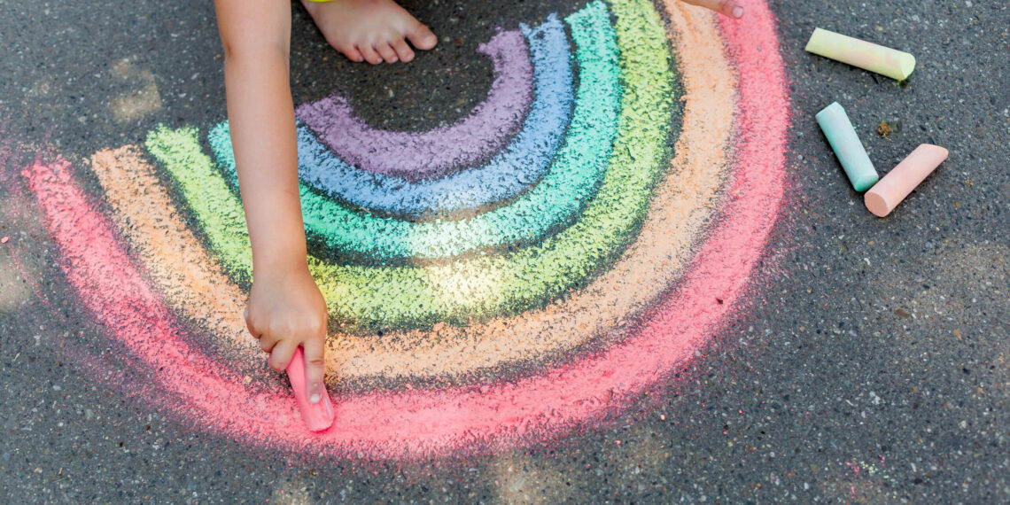 regenboog met stoepkrijt getekend Kind die een regenboog op de straat tekent met stoepkrijt