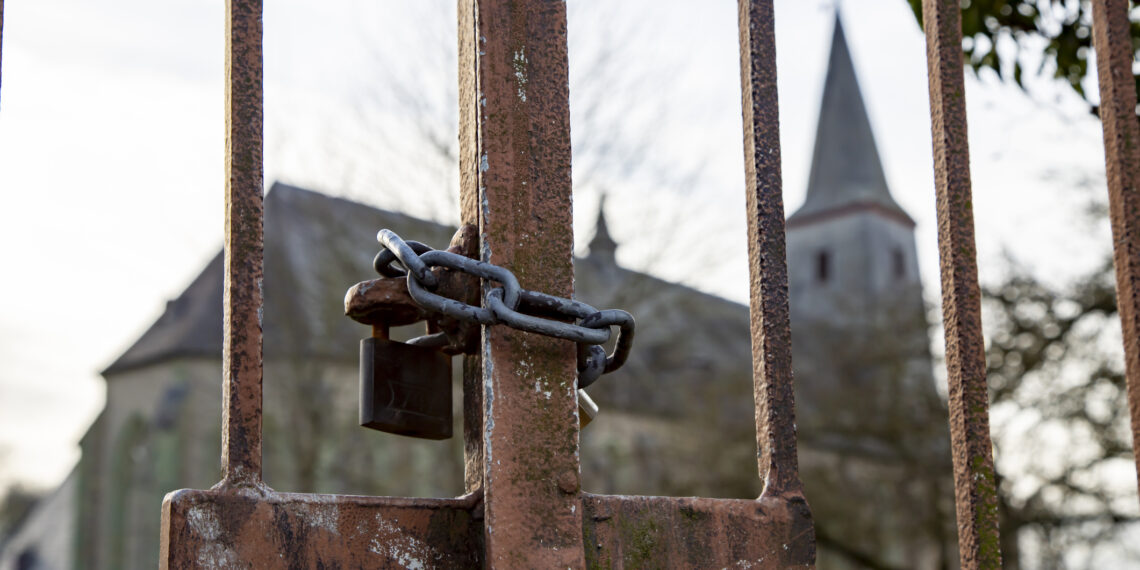 Kerkgebouw achter hek dat is afgesloten door een slot.