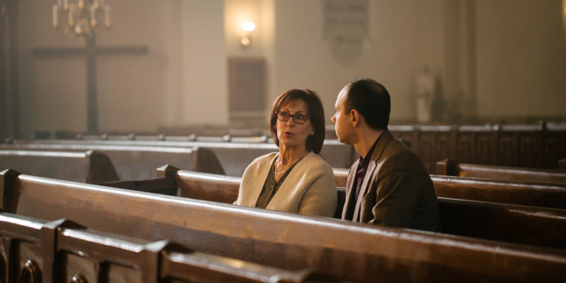 Portrait of Young Man and Old Woman Talking and Discussing While Sitting in a Church. Faithful Parishioners Seeking Comfort In Faith And Religious Beliefs, Consulting, Sharing Experiences and Wisdom Twee mensen met een gesprek in de kerk