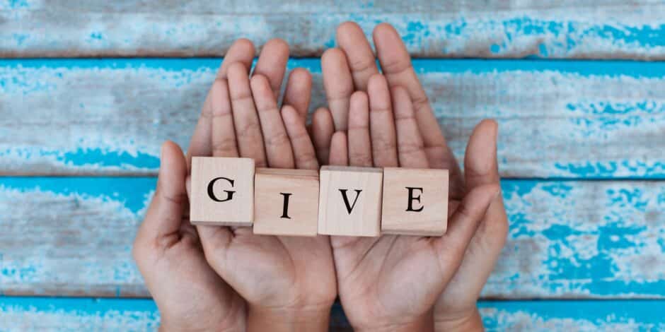 Handen in elkaar gevouwen met houten letters die het woord 'give' vormen