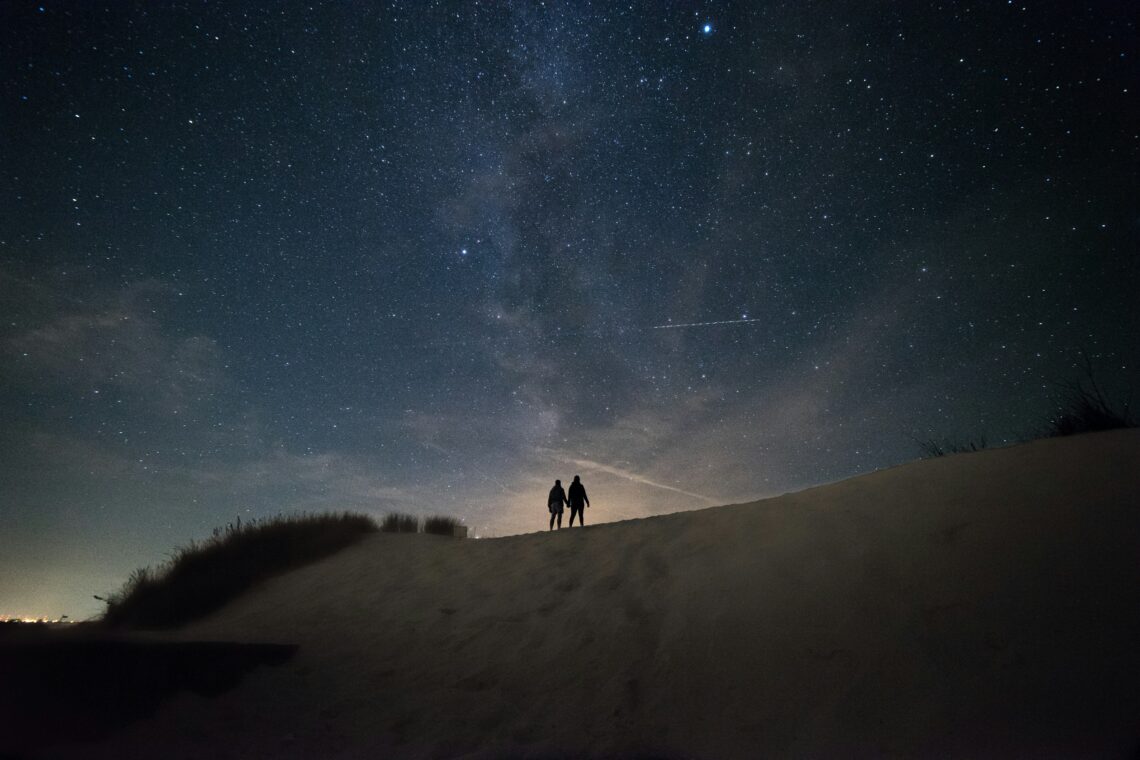 Mensen die hand in hand lopen in de duinen 's nachts