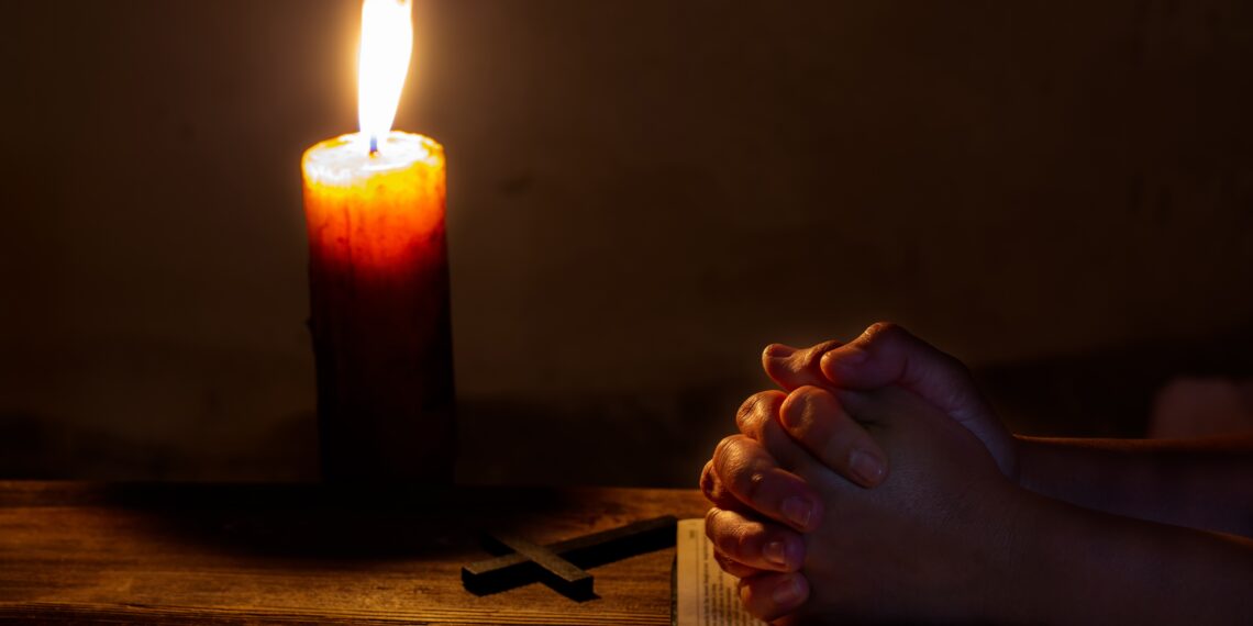 Biddende handen Bidden handen op een Bijbel met een kaars en een kruis ernaast