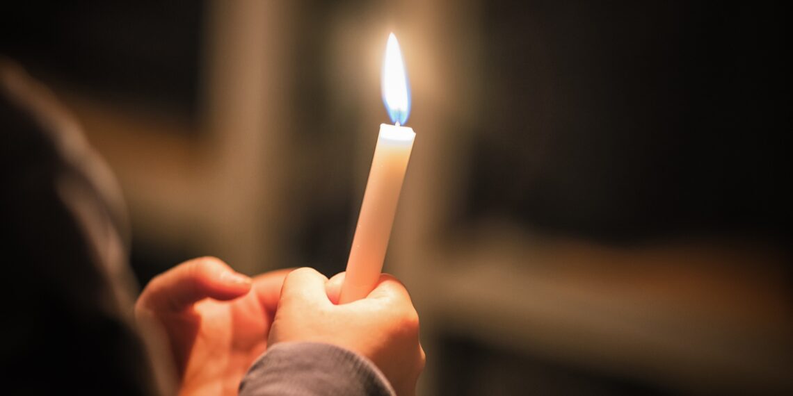Kaarsje Persoon die een kaarsje vasthoudt. In de achtergrond is een kruis te zien