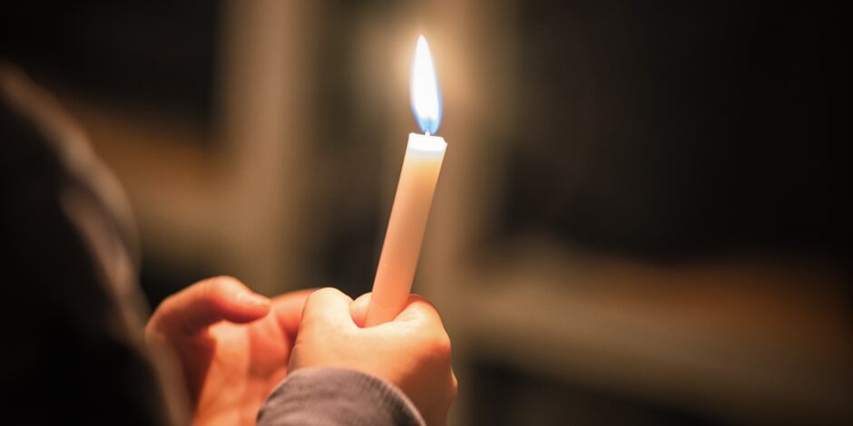 Persoon die een kaarsje vasthoudt. In de achtergrond is een kruis te zien