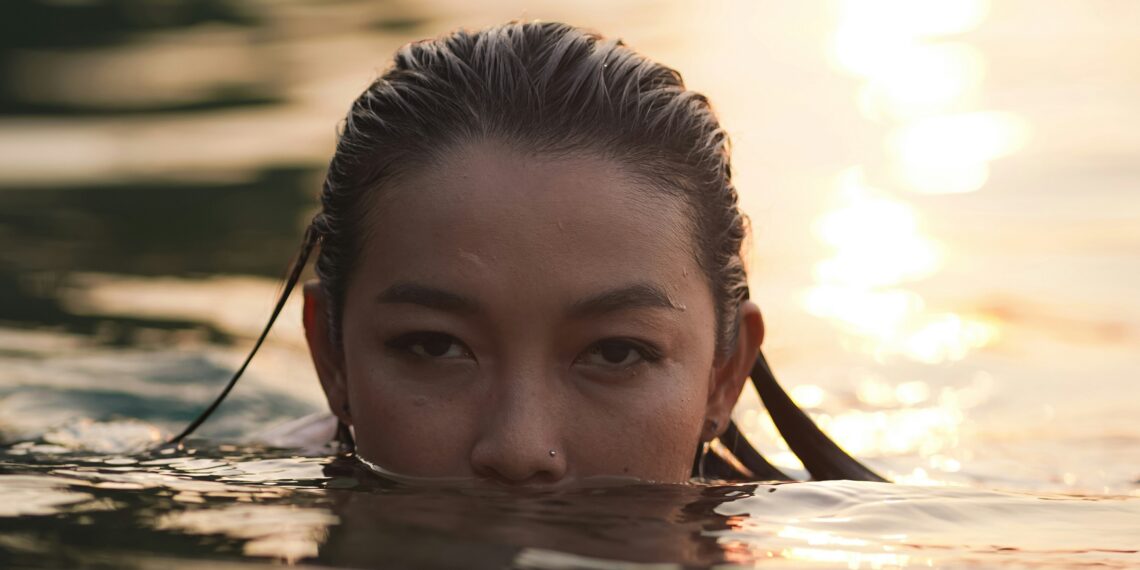 Close-up van een vrouw die in een rivier zwemt. Ze is met de helft van haar gezicht onder water.