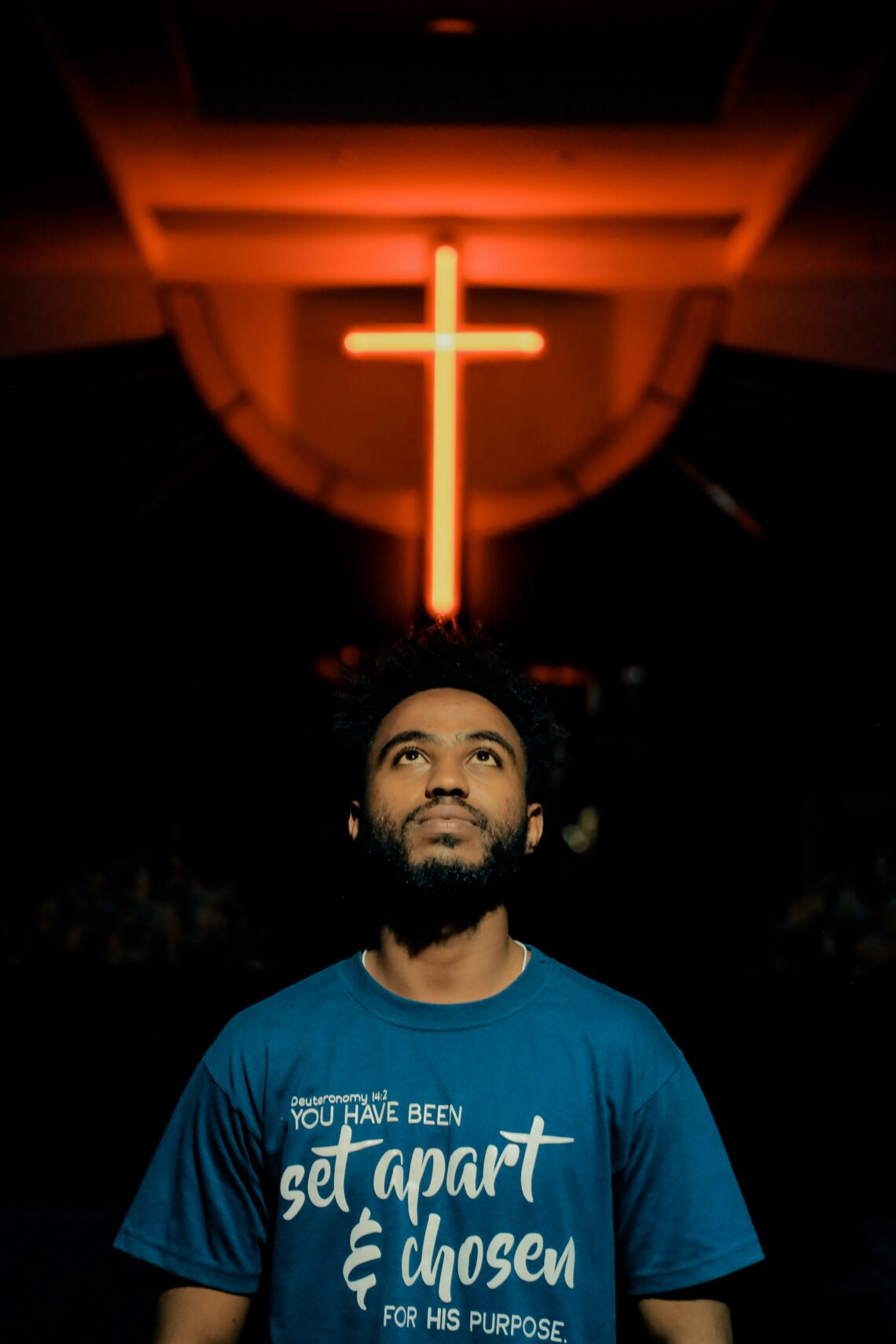 Man die omhoog kijkt. Achter hem is een oranje verlicht kruis te zien.