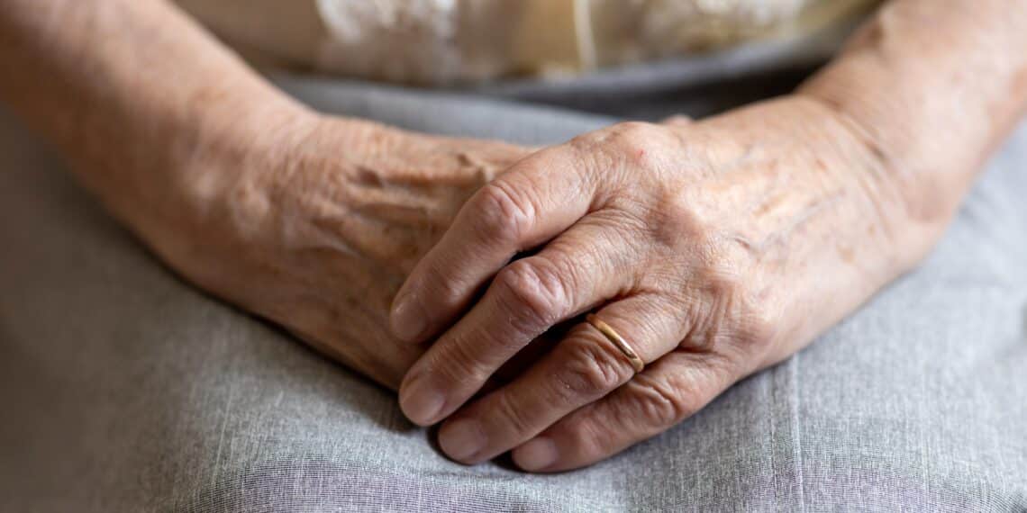 Oude vrouw die haar handen gevouwen op schoot heeft