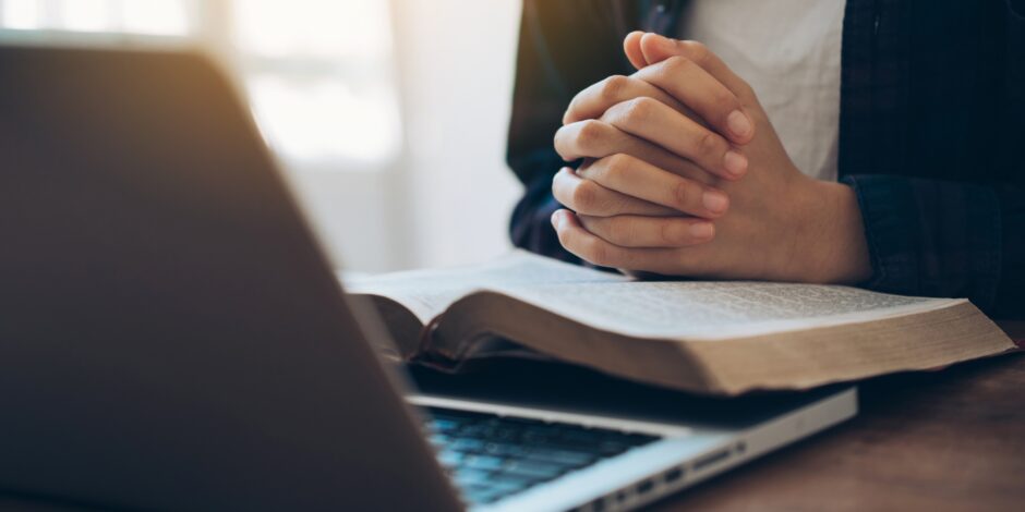 Vrouw heeft haar handen gevouwen op een bijbel gelegd terwijl ze op haar laptop kijkt