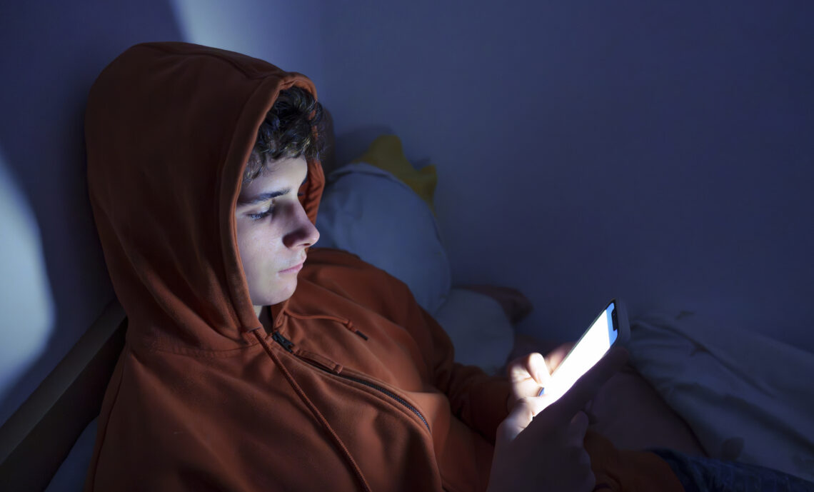 Tiener die in bed ligt en op zijn telefoon aan het scrollen is