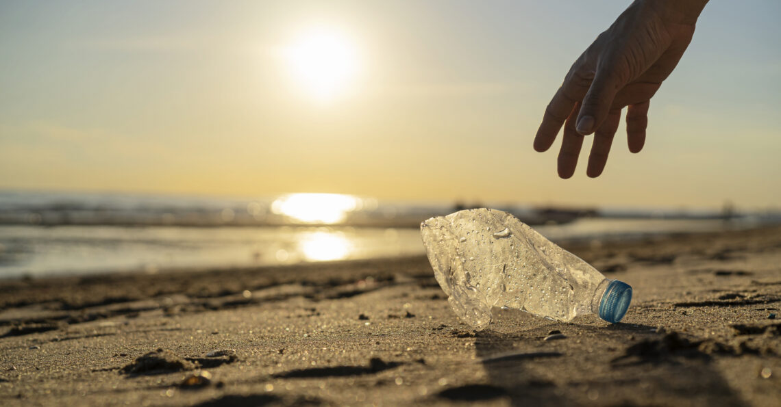 Persoon die een plastic flesje opruimt van het strand