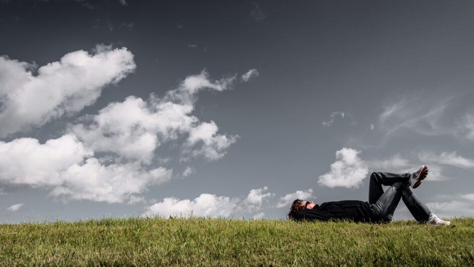 Man met sneakers ligt in het gras naar de wolken te kijken