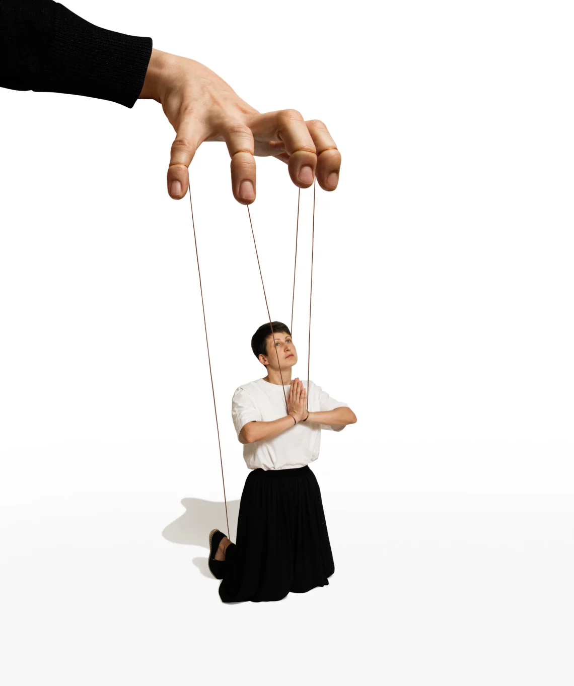 Vrouw met kort haar zit aan touwtjes vast die door een mannenhand bediend worden.