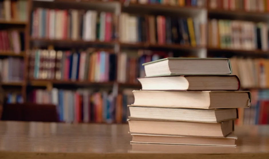 Stapel boeken met op de achtergrond een boekenkast